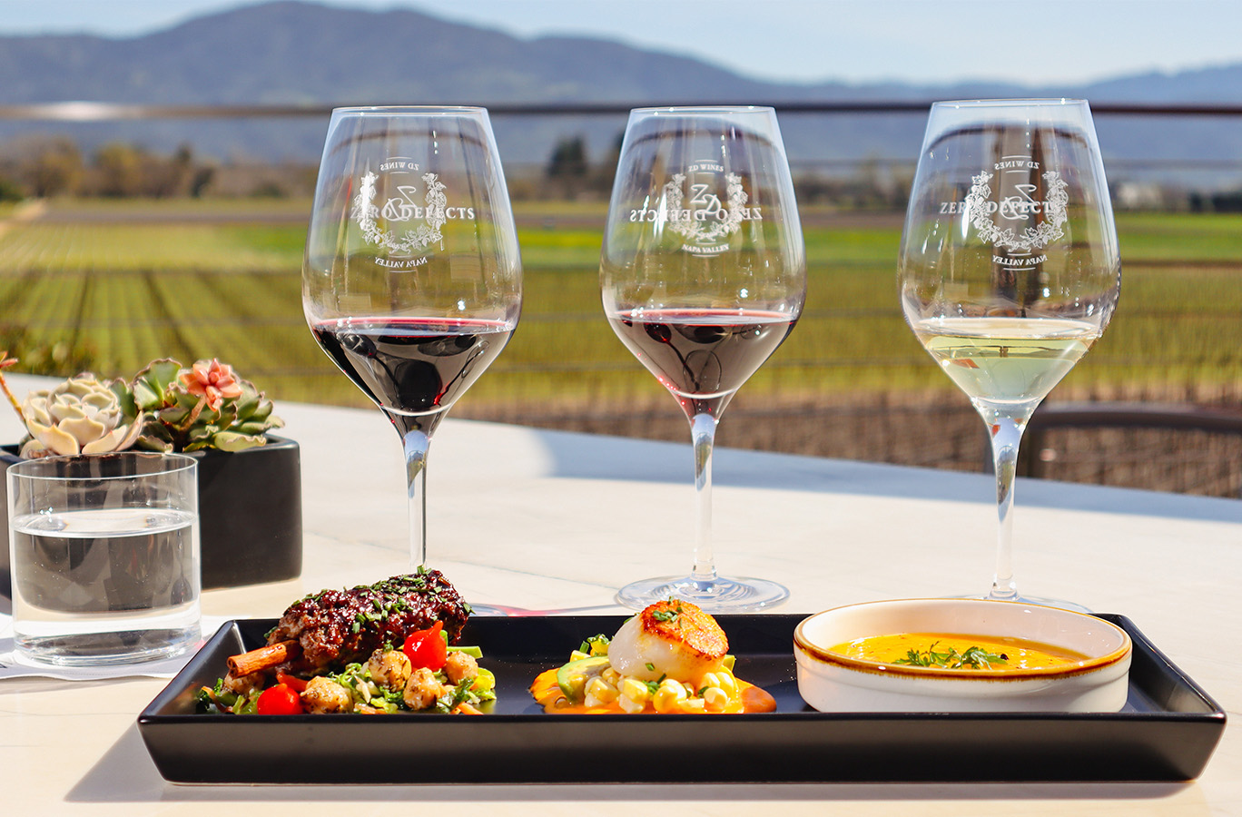 A trio of ZD wines and food pairings on a table overlooking Rutherford vineyards